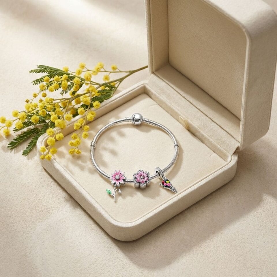 Bracciale charm con fiori e uccellino, gioielli eleganti e femminili, presentato in una scatola di velluto beige, decorato con fiori gialli, perfetto come regalo romantico o per occasioni speciali.