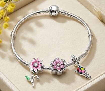 Bracciale charm con fiori e uccellino, gioielli eleganti e femminili, presentato in una scatola di velluto beige, decorato con fiori gialli, perfetto come regalo romantico o per occasioni speciali.